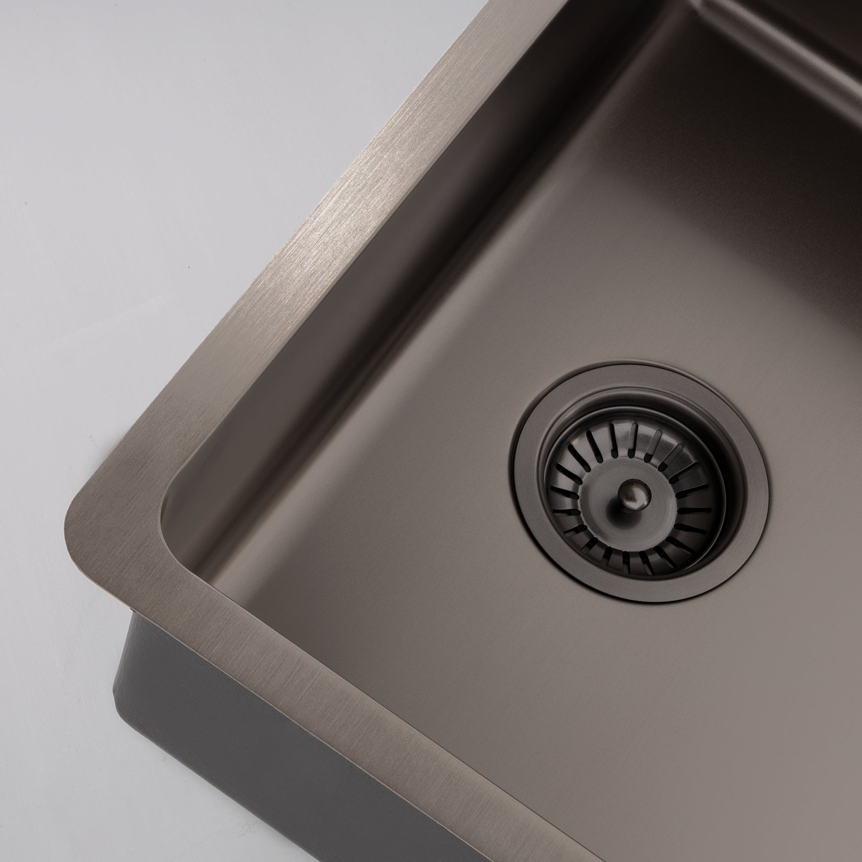 Close-up still life image of a Titan large bowl gunmetal sink against a gray background, highlighting the elegant design of the brass sink.