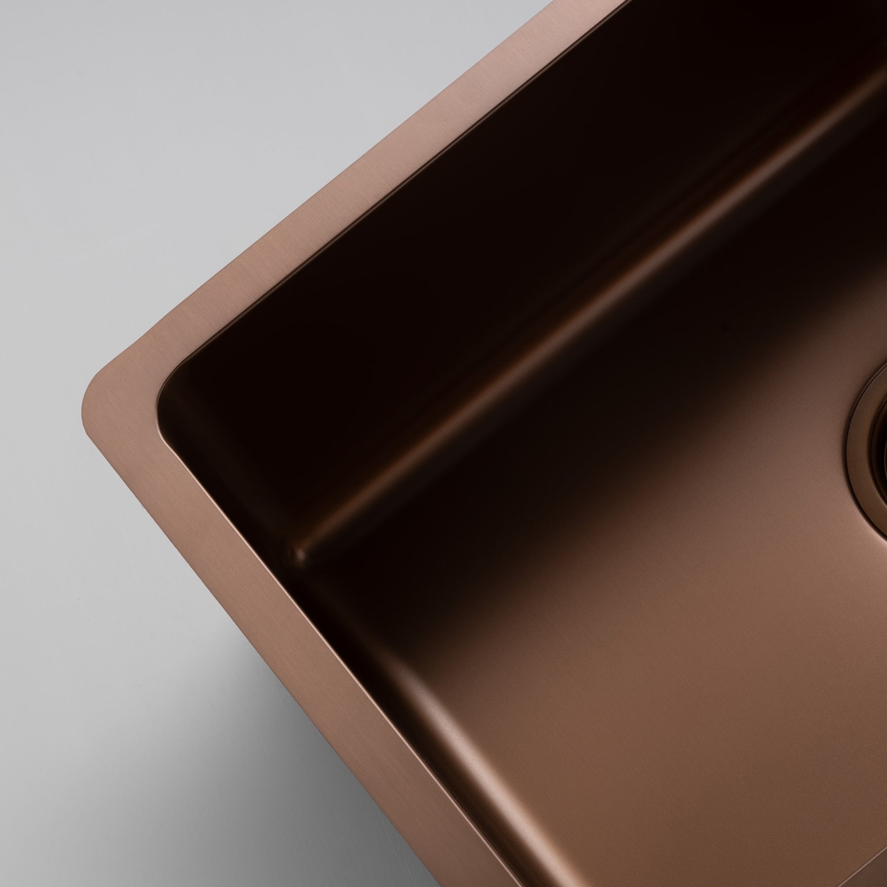 Close-up still life image of a Titan large bowl rose gold kitchen sink against a gray background, highlighting the elegant design of the brass sink.